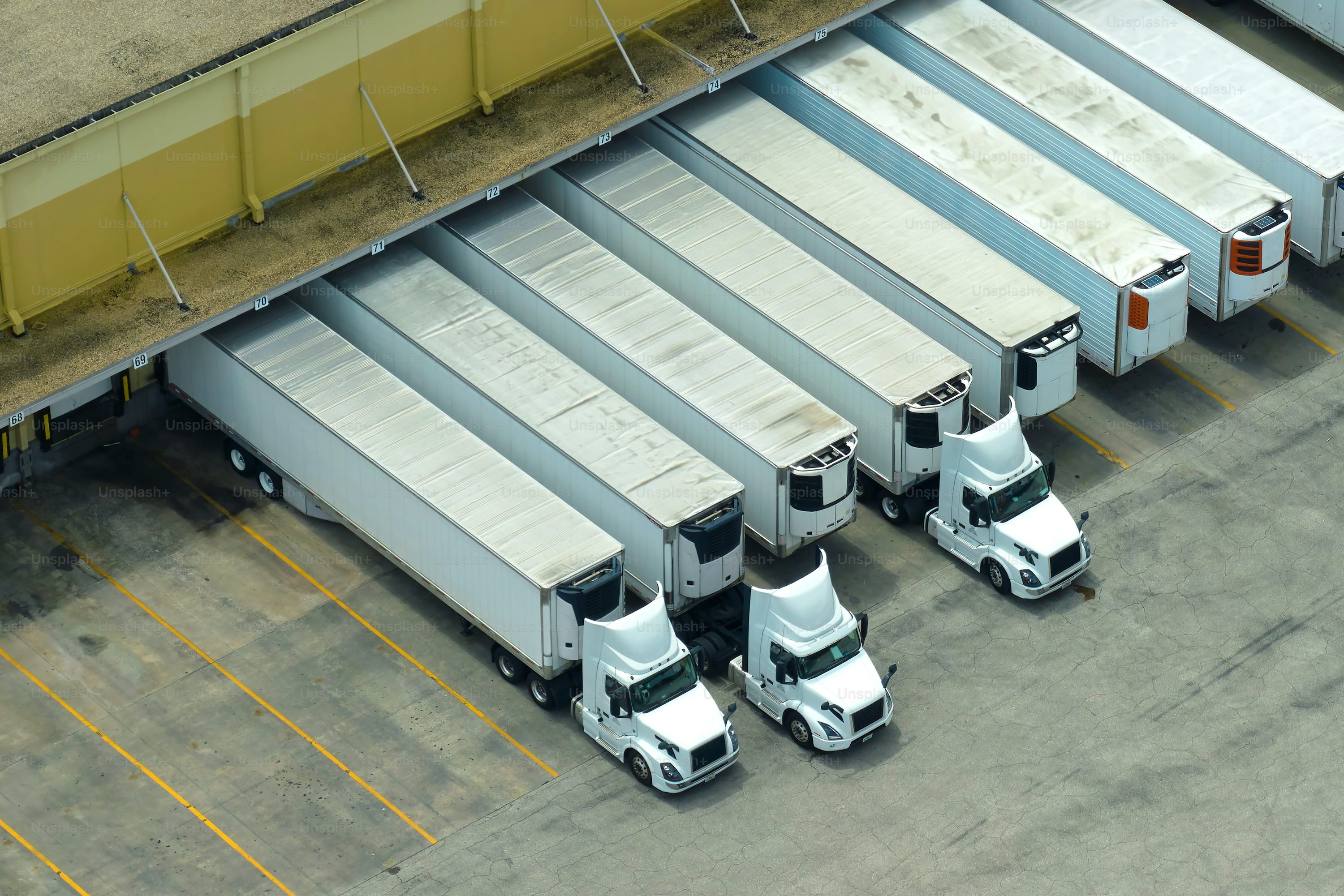 Big corporate shipment center with many cargo semi trucks unloading and uploading retail products for further retail shipment. Global market concept.