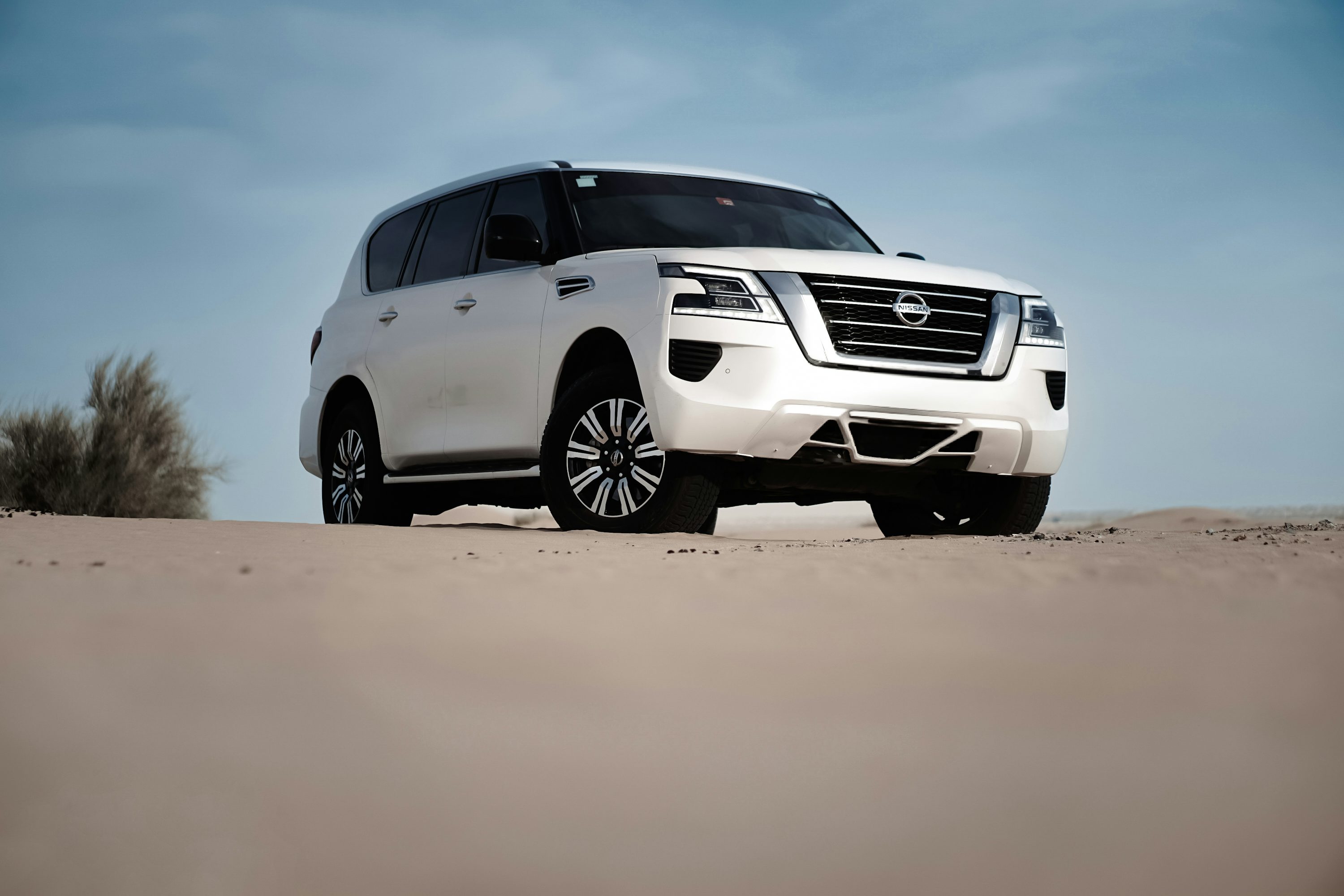 A white suv on sand, under a blue sky.