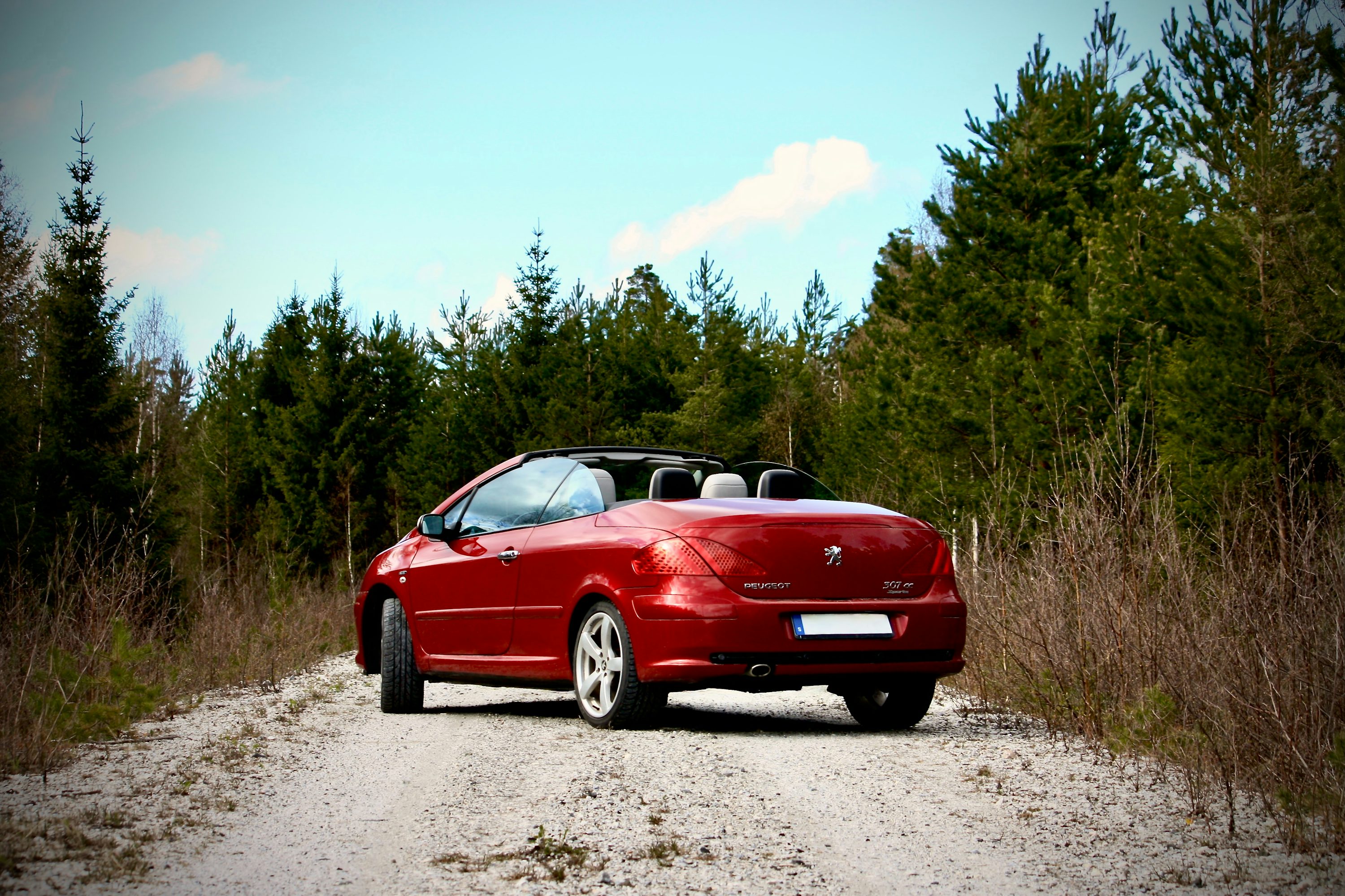 A red car parked on the side of a dirt road