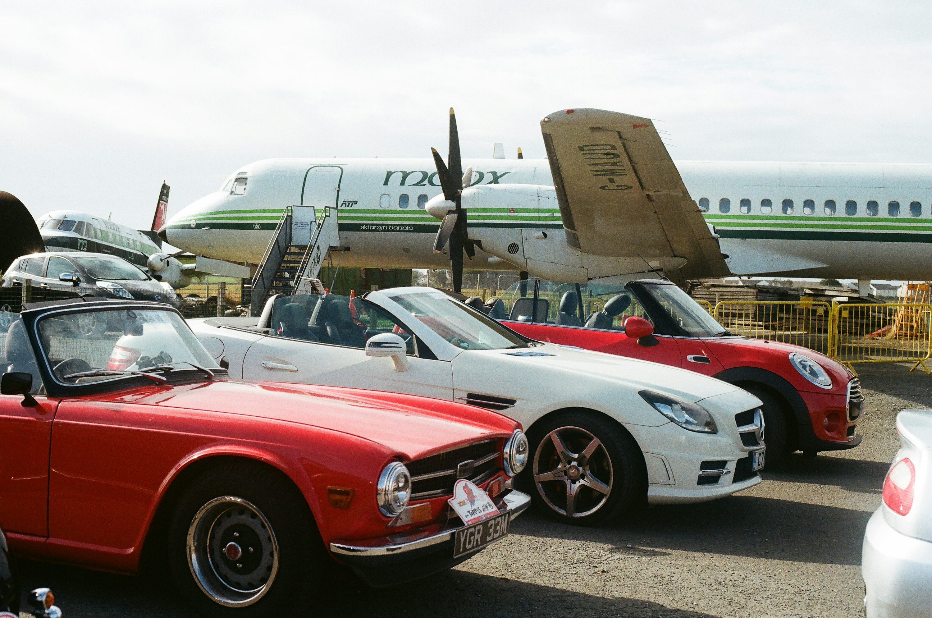 Convertible cars parked near an airplane