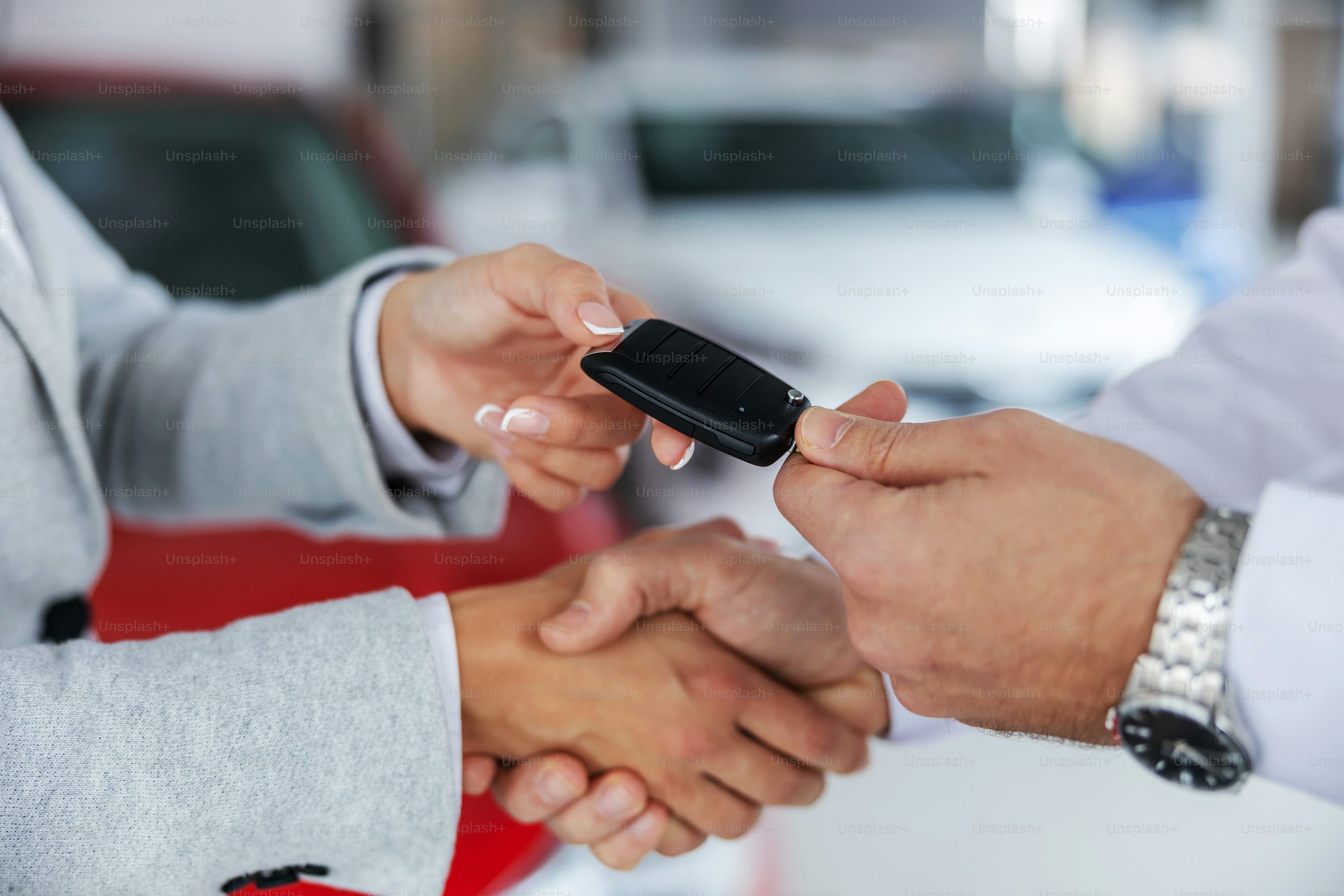 Closeup of car seller and a buyer shaking hands while standing in car salon. Seller handing car keys to a buyer.