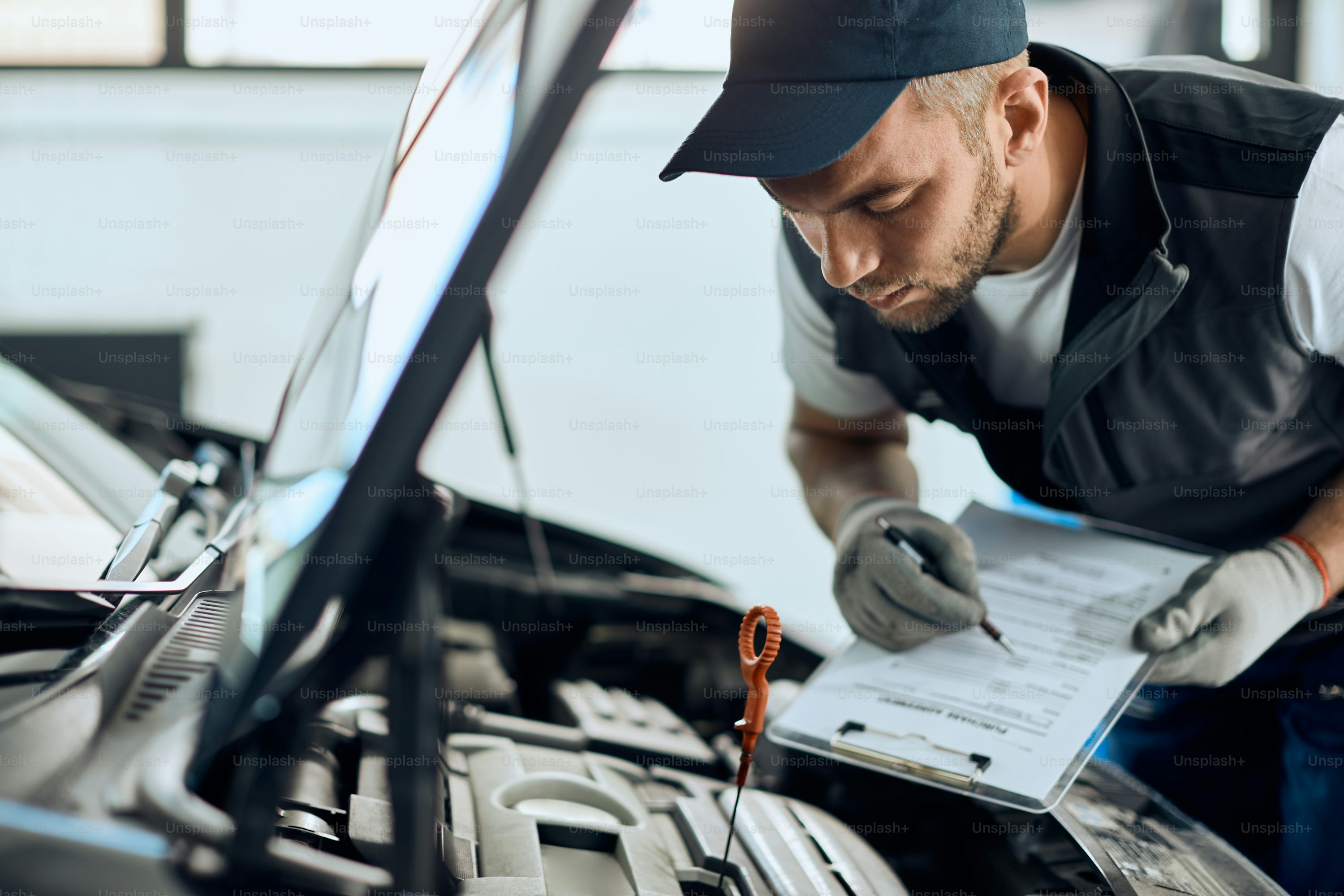 Young mechanic checking car oil and taking notes while working at auto repair shop.