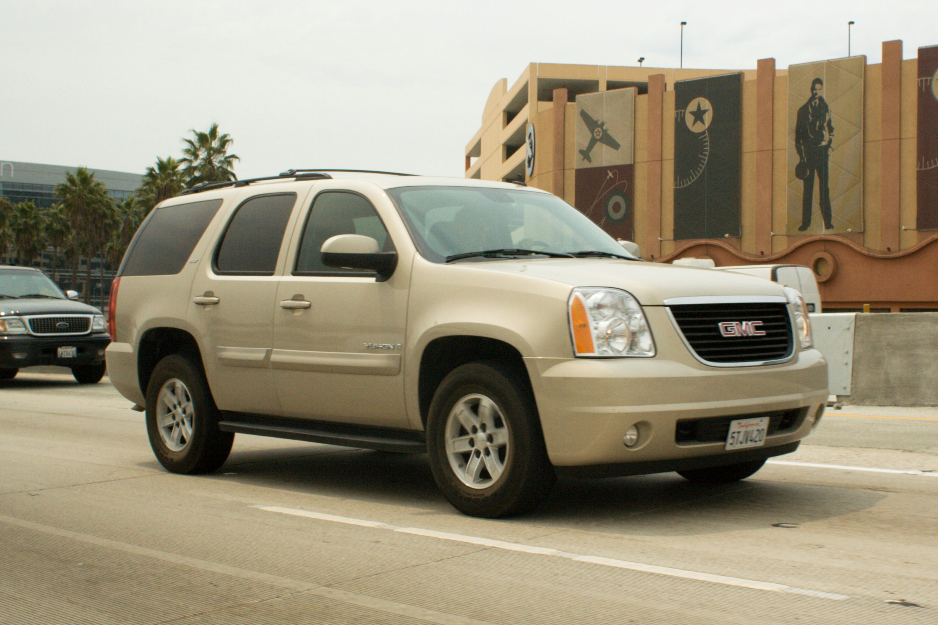 A tan gmc yukon suv driving on a highway.