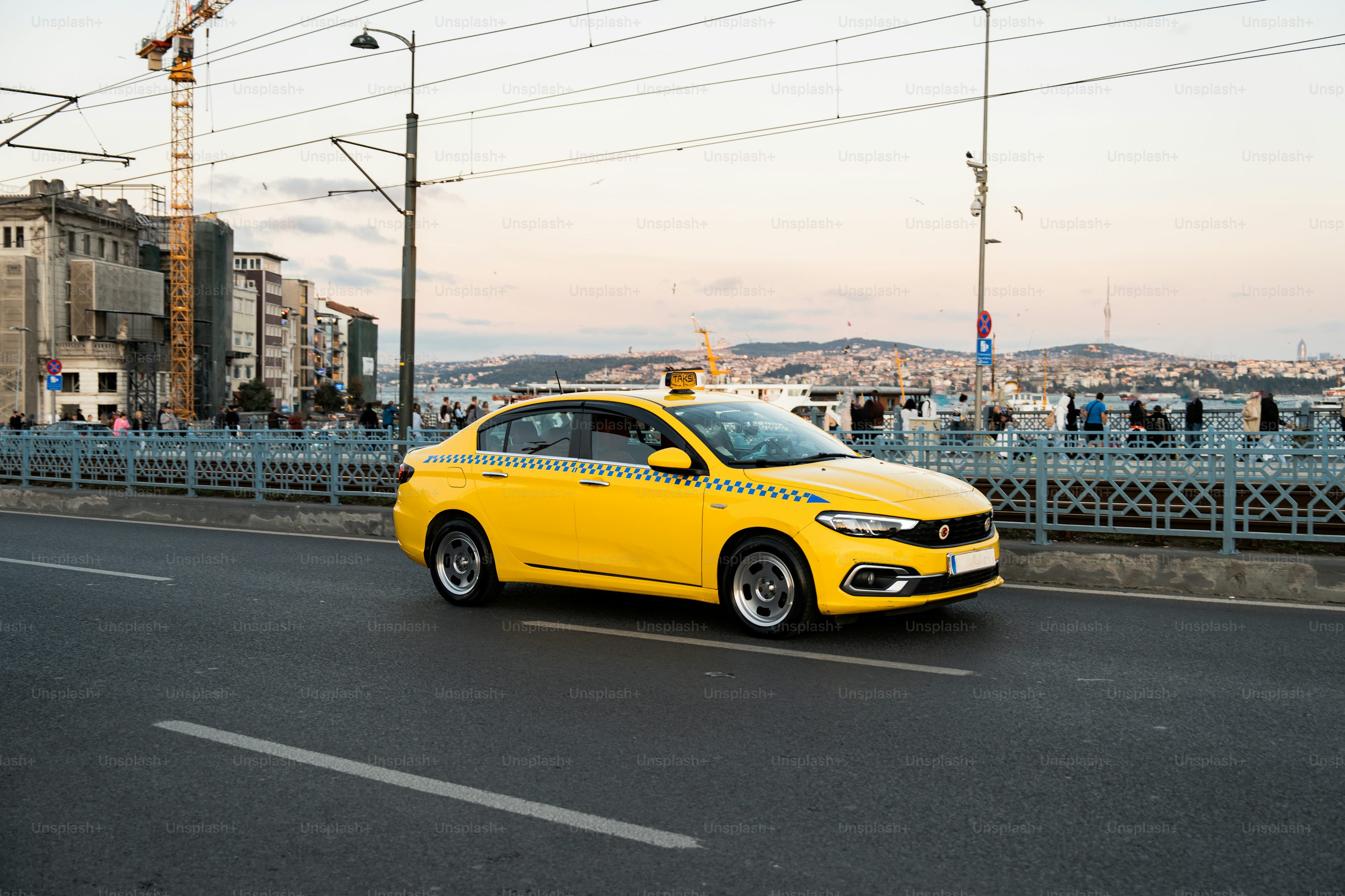 A yellow car driving down a street next to a bridge